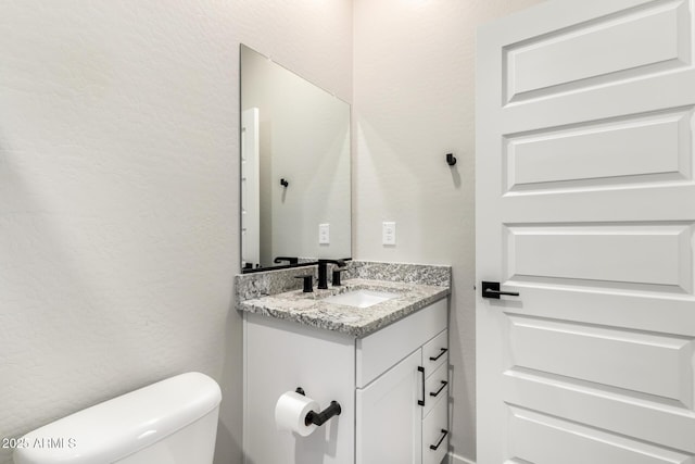 half bathroom featuring toilet, a textured wall, and vanity