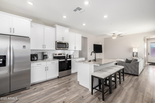 kitchen featuring a breakfast bar, stainless steel appliances, visible vents, decorative backsplash, and a sink