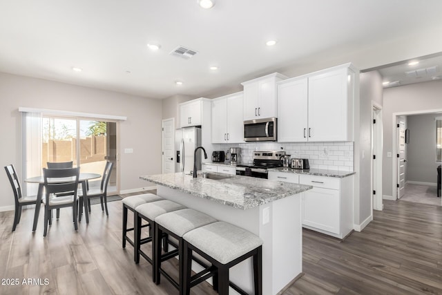 kitchen featuring tasteful backsplash, visible vents, appliances with stainless steel finishes, a sink, and an island with sink