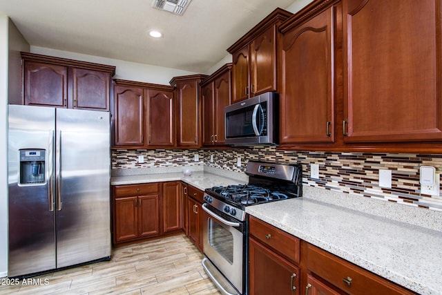 42531 W Heavenly Pl, Maricopa, AZ 85138 - kitchen with visible vents, decorative backsplash, appliances with stainless steel finishes, light wood-style floors, and light stone countertops