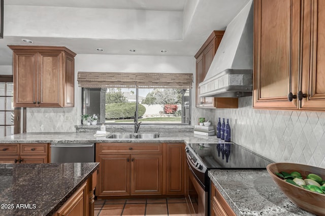 kitchen featuring sink, light tile patterned floors, appliances with stainless steel finishes, dark stone countertops, and premium range hood