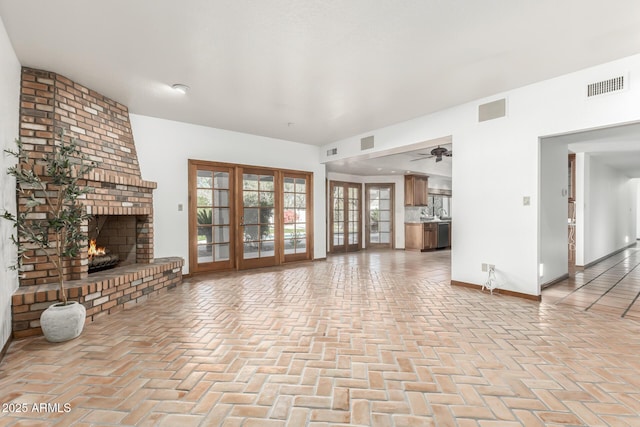 unfurnished living room featuring a brick fireplace, french doors, and ceiling fan