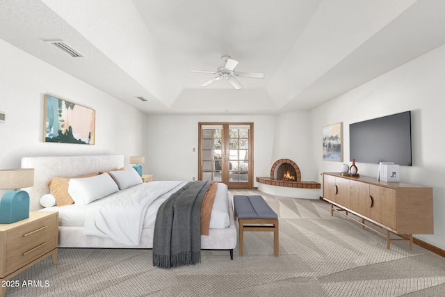 carpeted bedroom with french doors, ceiling fan, a raised ceiling, and a large fireplace