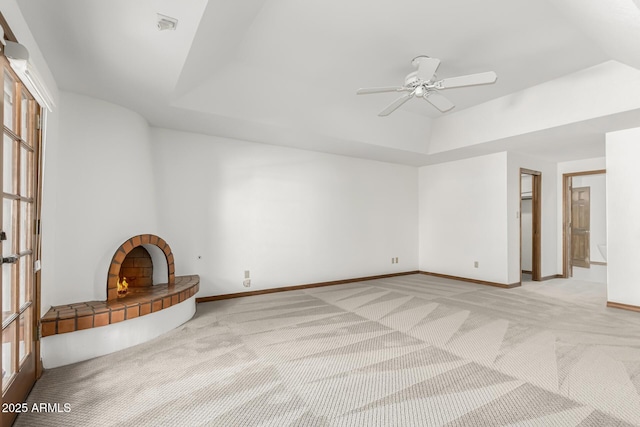 unfurnished living room featuring light carpet, a tile fireplace, a raised ceiling, and ceiling fan