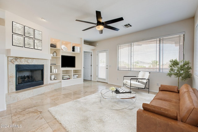 living room featuring built in shelves, a premium fireplace, and ceiling fan