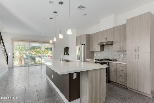 kitchen featuring light countertops, backsplash, appliances with stainless steel finishes, a sink, and under cabinet range hood