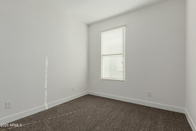 spare room with baseboards and dark colored carpet