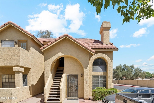 exterior space featuring a tiled roof, a chimney, stairway, fence, and stucco siding