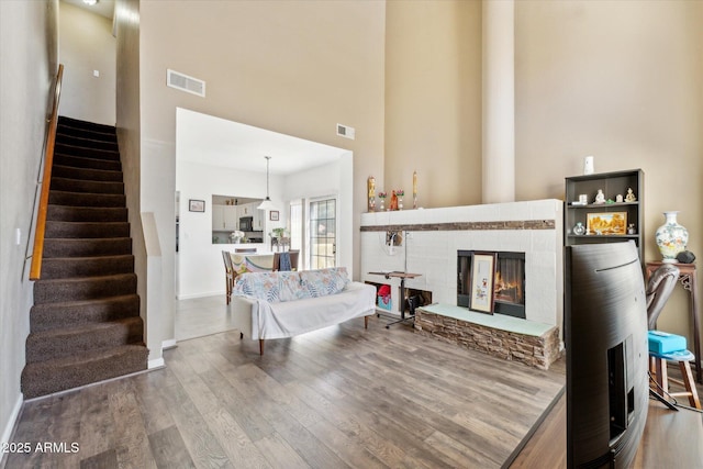 living area featuring visible vents, a glass covered fireplace, a towering ceiling, and wood finished floors