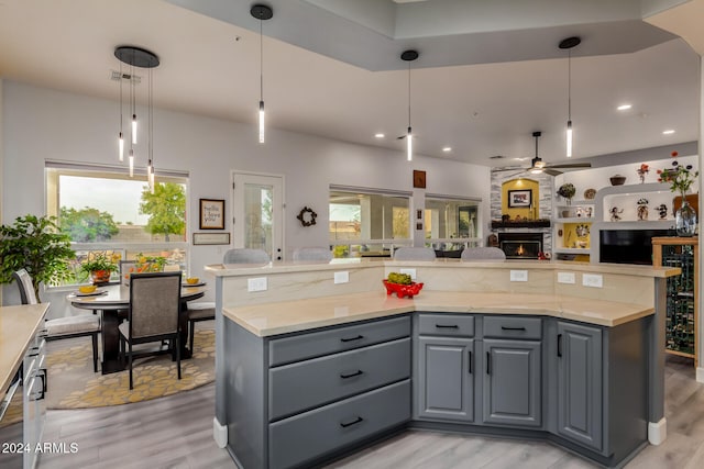 kitchen with gray cabinets, a stone fireplace, hanging light fixtures, and a healthy amount of sunlight