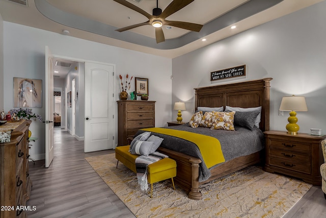 bedroom with a tray ceiling, ceiling fan, and light wood-type flooring