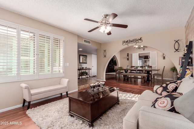 living room with wood finished floors, visible vents, arched walkways, ceiling fan, and a textured ceiling