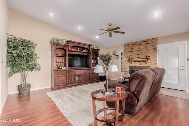 living area featuring wood finished floors, a ceiling fan, baseboards, lofted ceiling, and a large fireplace