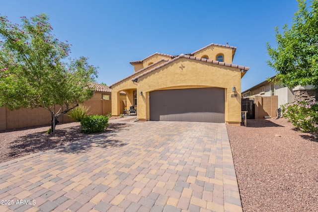 mediterranean / spanish-style home with a garage, fence, decorative driveway, stucco siding, and a tiled roof