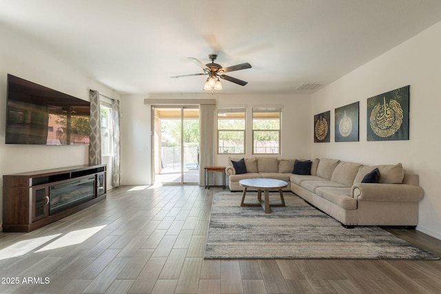 living room with visible vents, a glass covered fireplace, ceiling fan, and wood finished floors