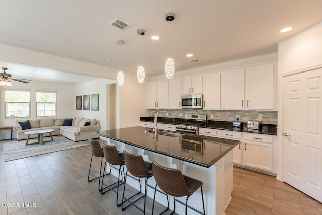 kitchen featuring a kitchen bar, visible vents, appliances with stainless steel finishes, a sink, and white cabinetry