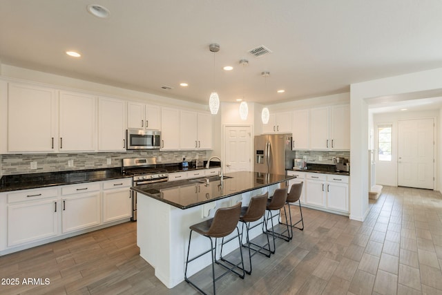 kitchen featuring visible vents, a kitchen breakfast bar, a sink, appliances with stainless steel finishes, and backsplash