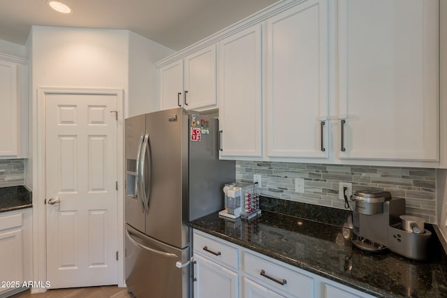 kitchen featuring stainless steel fridge, white cabinetry, dark stone countertops, and tasteful backsplash
