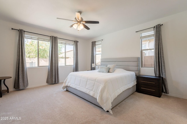 bedroom featuring light colored carpet, baseboards, ceiling fan, and multiple windows
