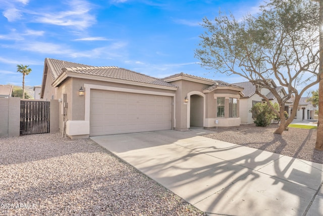 mediterranean / spanish-style home with an attached garage, a tiled roof, concrete driveway, a gate, and stucco siding