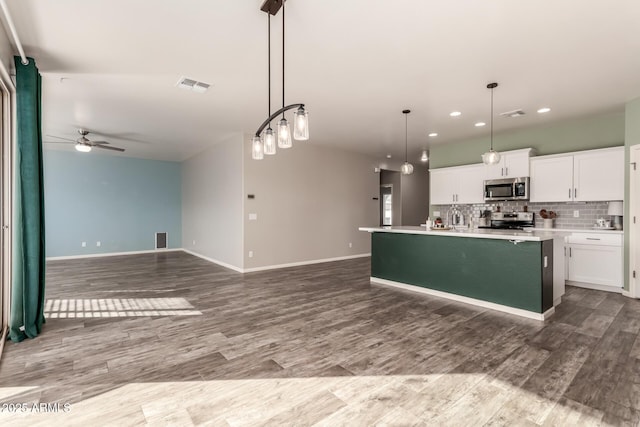 kitchen featuring ceiling fan, hanging light fixtures, stainless steel appliances, a center island with sink, and white cabinets