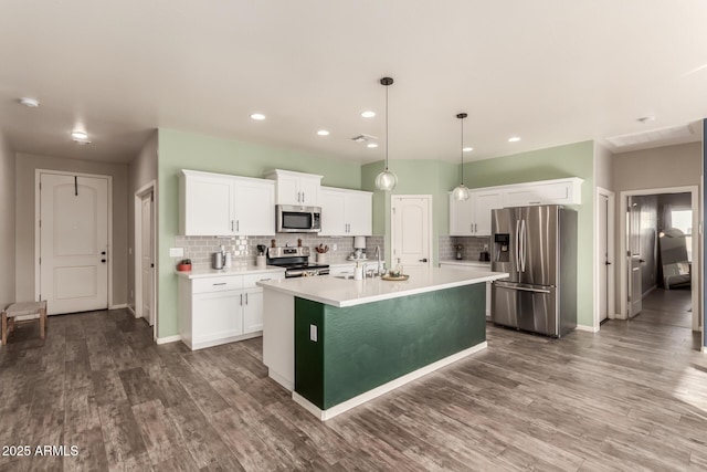 kitchen with dark wood-type flooring, hanging light fixtures, stainless steel appliances, an island with sink, and white cabinets