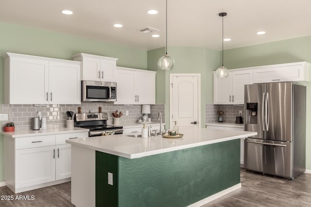 kitchen featuring pendant lighting, a center island with sink, white cabinets, wood-type flooring, and stainless steel appliances