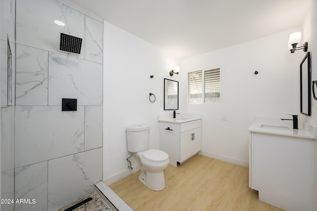 bathroom with hardwood / wood-style flooring, vanity, toilet, and tiled shower
