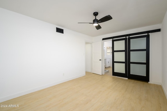 unfurnished bedroom featuring a barn door, light hardwood / wood-style floors, and ceiling fan