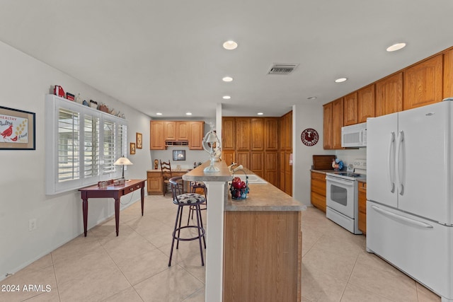 kitchen featuring a kitchen breakfast bar, light tile floors, a center island, white appliances, and sink