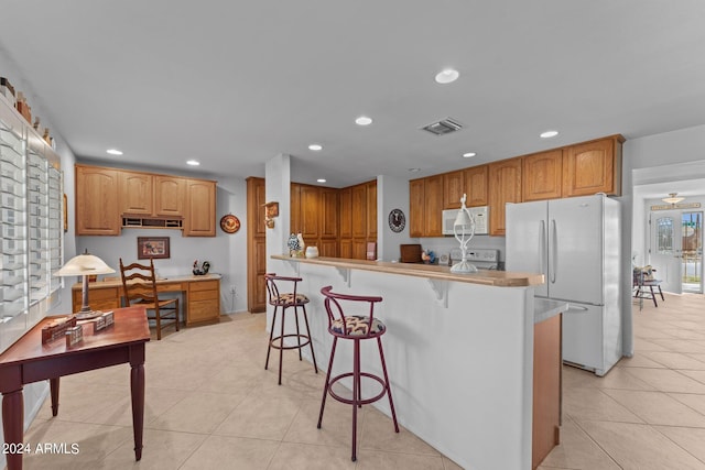 kitchen with white appliances, a breakfast bar, ceiling fan, and light tile floors