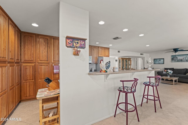 kitchen with ceiling fan, a breakfast bar area, light tile floors, white refrigerator, and kitchen peninsula