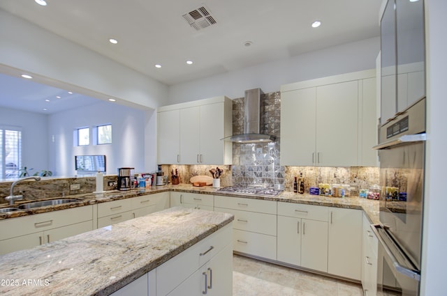 kitchen featuring sink, wall chimney exhaust hood, decorative backsplash, light stone countertops, and stainless steel appliances