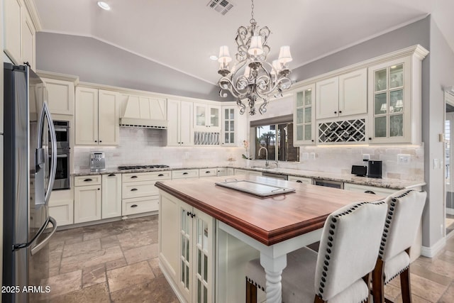 kitchen featuring stainless steel appliances, a center island, a kitchen breakfast bar, wood counters, and decorative light fixtures