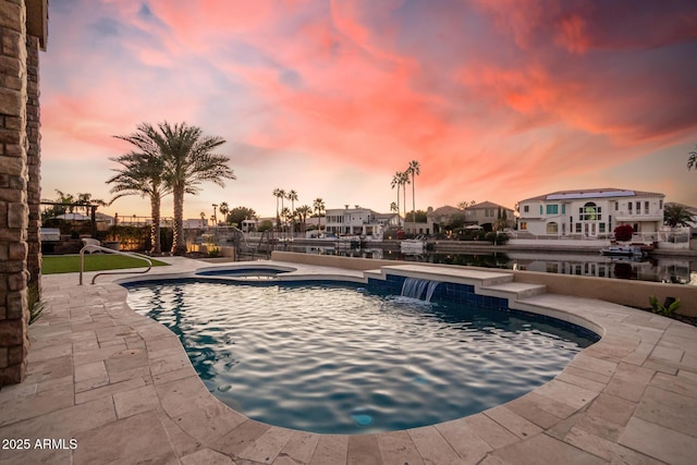 pool at dusk featuring pool water feature and an in ground hot tub