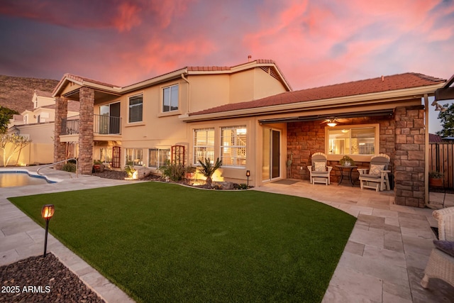 back house at dusk featuring a fenced in pool, a patio, a balcony, and a yard