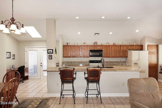 kitchen with light tile patterned floors, pendant lighting, white refrigerator with ice dispenser, and light stone counters