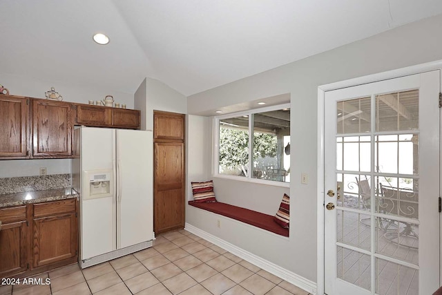 kitchen featuring white fridge with ice dispenser, light tile patterned flooring, and lofted ceiling