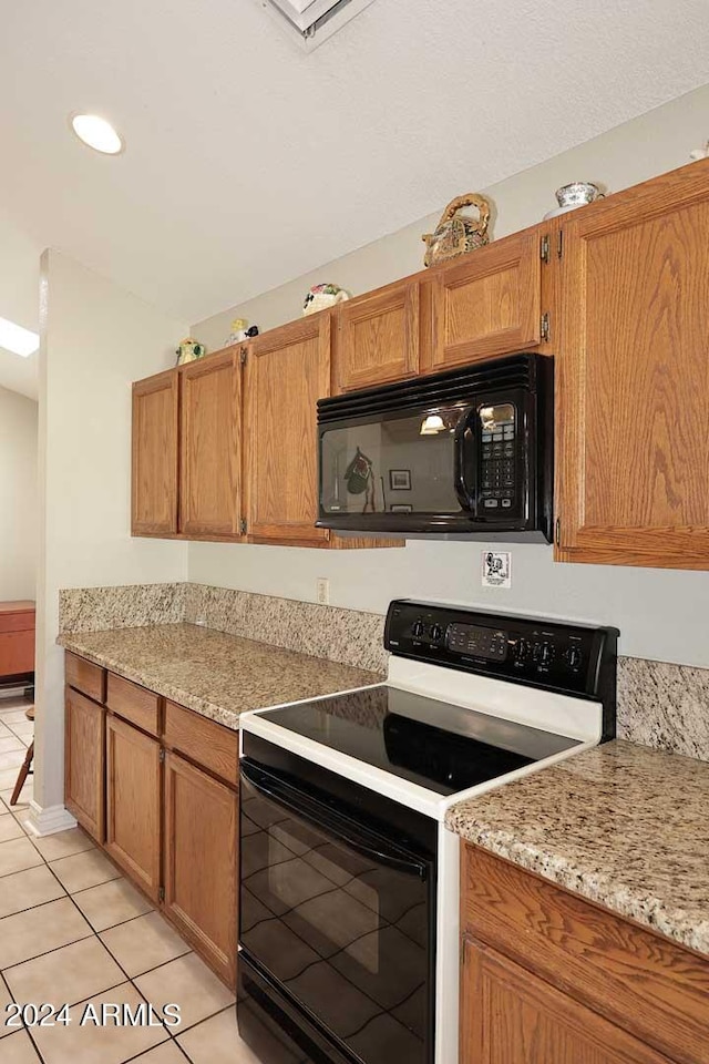 kitchen featuring light tile patterned flooring, black appliances, and light stone counters