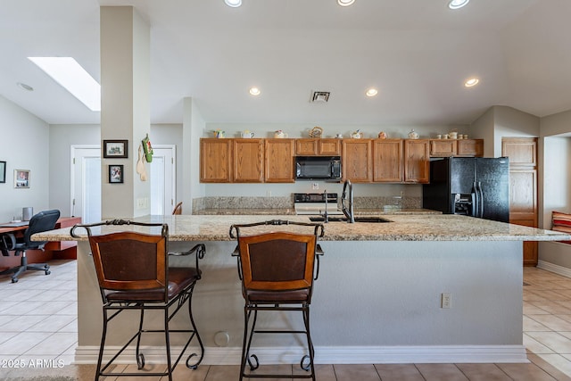 kitchen featuring sink, black appliances, light tile patterned floors, and a spacious island