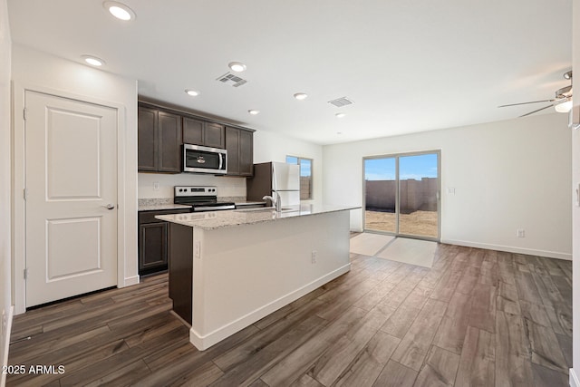 kitchen featuring dark brown cabinetry, a center island with sink, visible vents, appliances with stainless steel finishes, and dark wood-type flooring