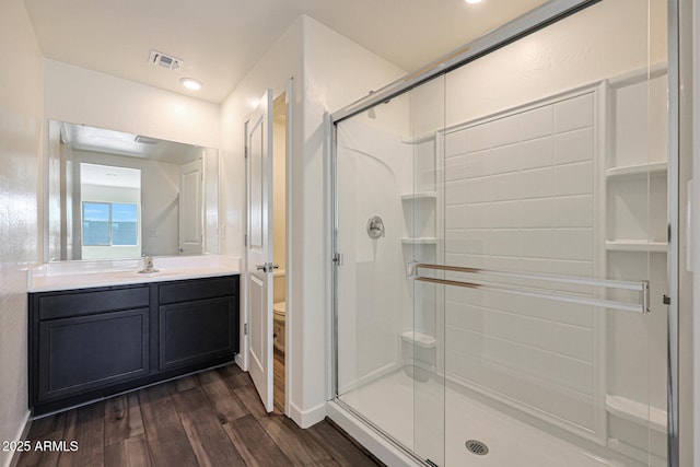 bathroom with a stall shower, toilet, wood finished floors, vanity, and recessed lighting