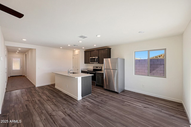 kitchen featuring an island with sink, dark wood-type flooring, stainless steel appliances, light countertops, and a sink