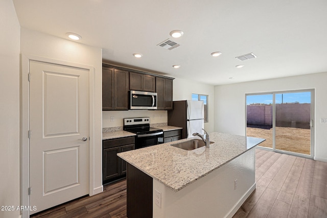 kitchen featuring visible vents, an island with sink, light stone counters, stainless steel appliances, and a sink