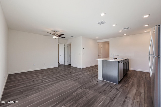 kitchen featuring a kitchen island with sink, open floor plan, light countertops, appliances with stainless steel finishes, and dark wood-style floors