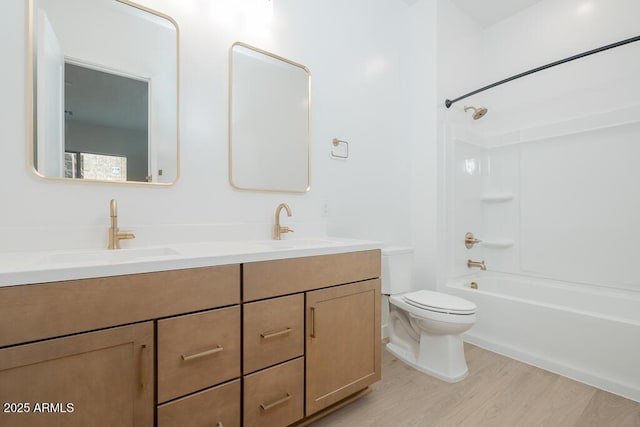 bathroom featuring toilet, double vanity, a sink, and wood finished floors