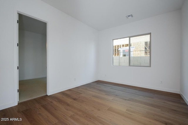 spare room featuring baseboards, visible vents, and wood finished floors