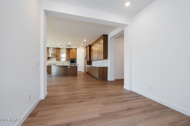 hallway with light wood finished floors, recessed lighting, a sink, and baseboards