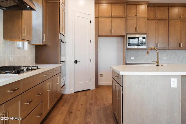 kitchen with stainless steel appliances, light countertops, light wood-type flooring, brown cabinetry, and backsplash