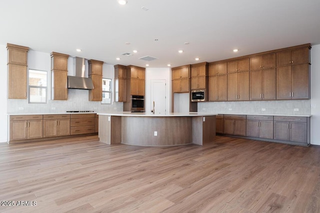 kitchen featuring appliances with stainless steel finishes, decorative backsplash, light wood-style flooring, and wall chimney exhaust hood